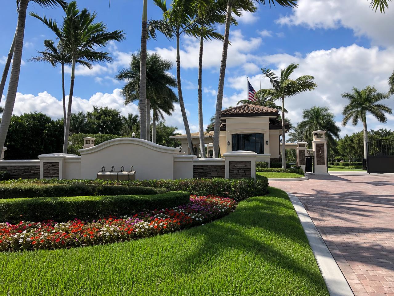 Maintained gated community entrance in Palm Beach County with royal palms and trimmed hedges