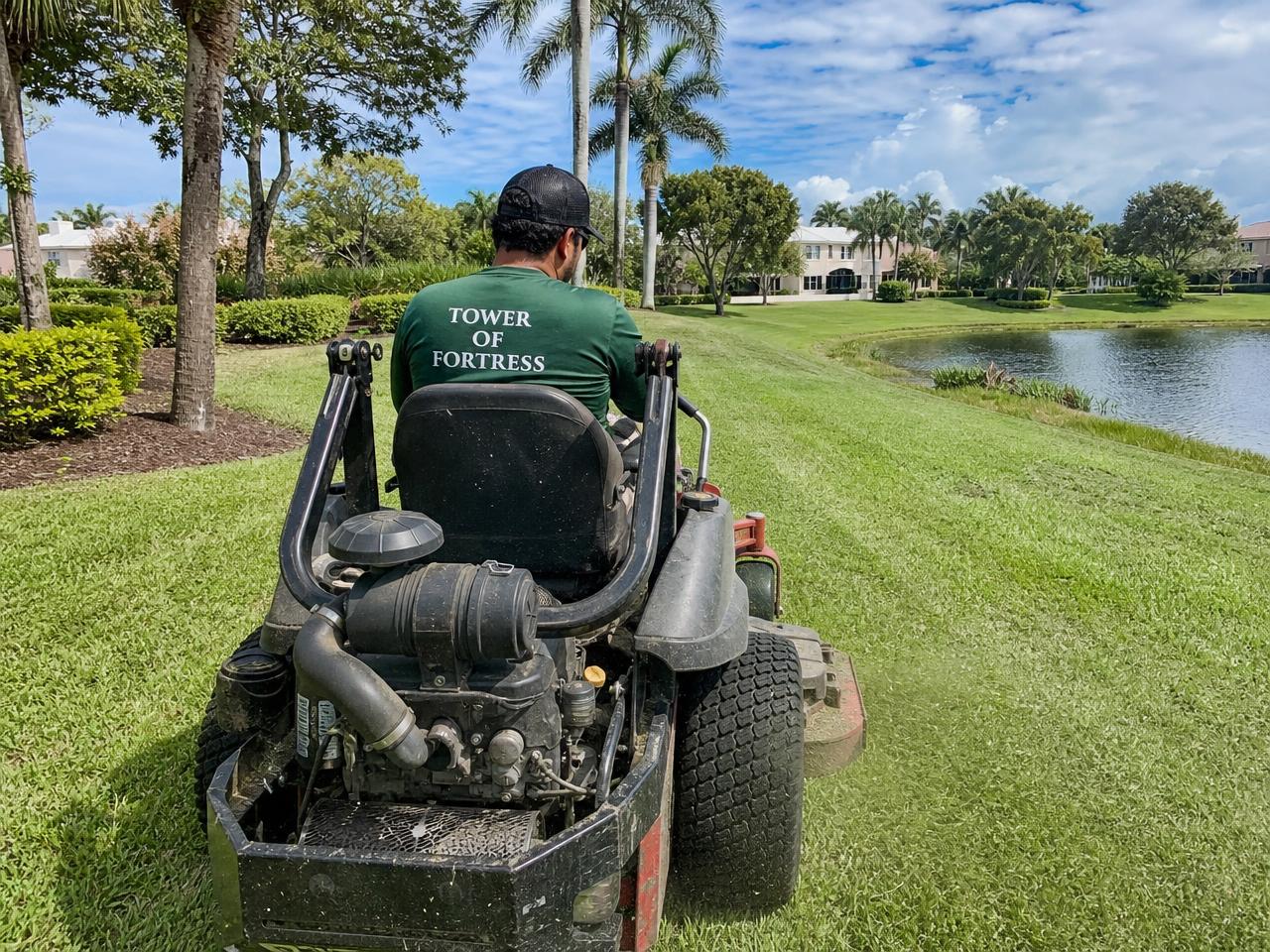 Landscape crew member mowing a community common area with a commercial zero-turn mower in Palm Beach County